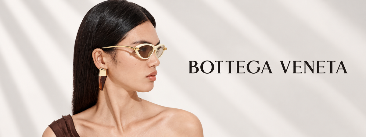 A woman in profile wearing Bottega Veneta sunglasses with gold-toned metal frames and translucent dark lenses, set against a light gray background with diagonal shadows and the Bottega Veneta brand name printed on the right.